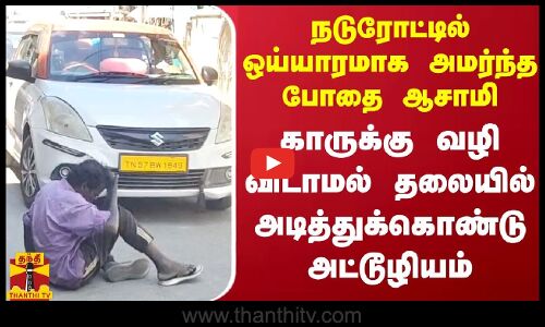 நடுரோட்டில் ஒய்யாரமாக அமர்ந்த போதை ஆசாமி காருக்கு வழி விடாமல் தலையில் அடித்துக்கொண்டு அட்டூழியம்